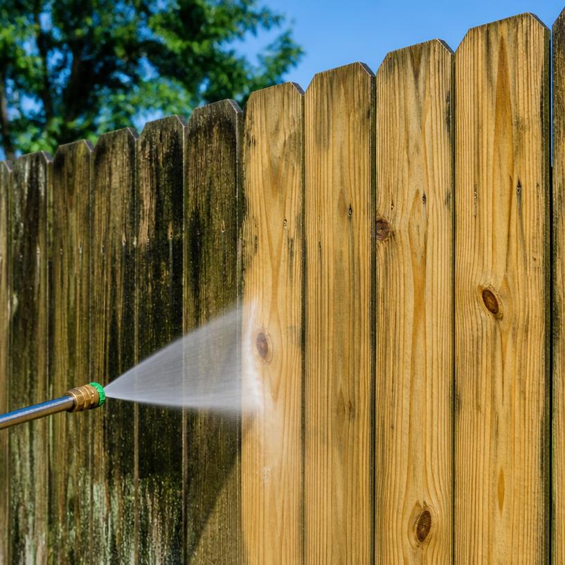 Pressure washer cleaning a weathered wooden fence